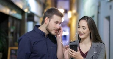 Gecenin içinde bir akıllı telefon müzik paylaşımı sokakta kameraya doğru yürüyen mutlu bir çift önden görünümü
