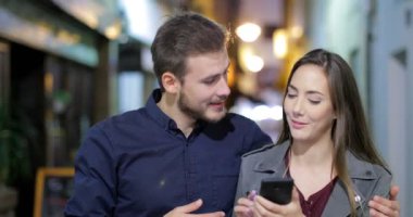 Eski bir şehir sokak gecede bir akıllı telefon kullanarak yürüyen bir mutlu çifti önden görünüm