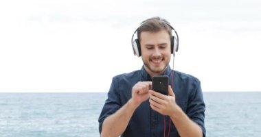 Tarama ve sahilde bir akıllı telefondan müzik dinlerken mutlu bir adam önden görünümü
