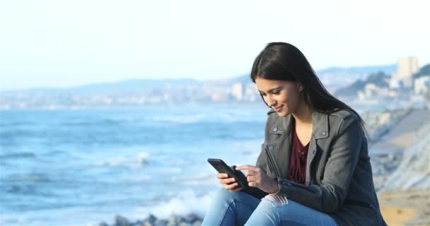 Feliz Adolescente Navegando Por Contenido Del Teléfono Inteligente Sentado Playa — Vídeo de stock