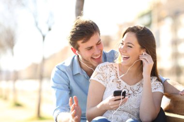 Birlikte online müzik dinleyen neşeli bir çift parkta bir bankta oturuyor.