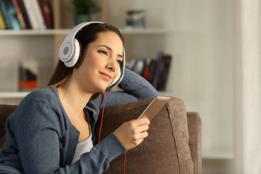 Relaxed woman listening chillout music sitting on a couch in the living room at home clipart