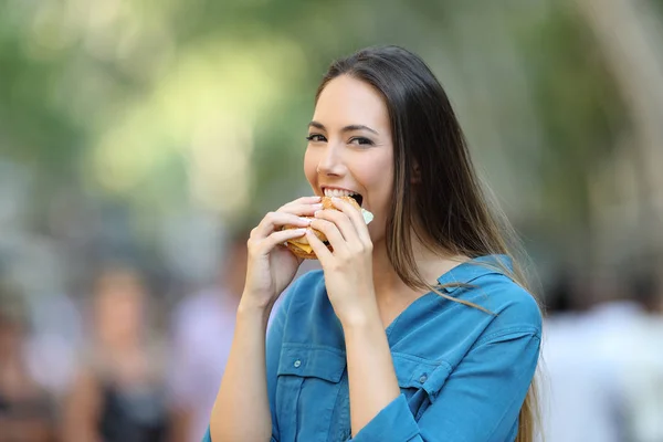 通りでカメラ目線バーガーをかむ幸せな女 — ストック写真