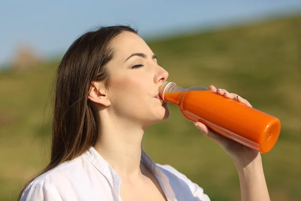 公園の空瓶からオレンジジュースを飲む女性 — ストック写真