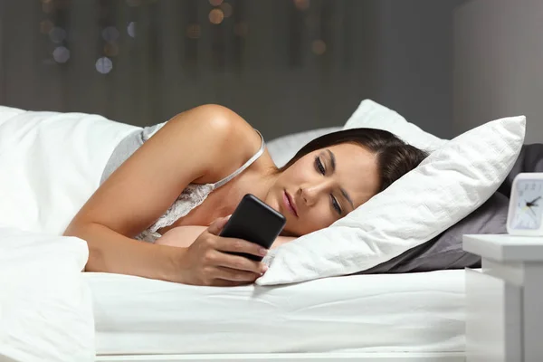 Серьёзная Женщина Проверяет Содержимое Смартфона Лежащего Кровати Ночью Дома — стоковое фото