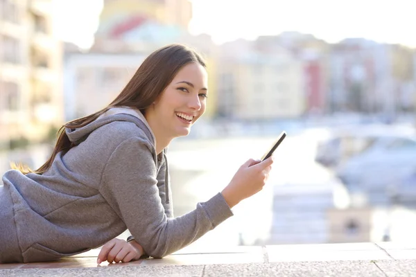 Šťastný Dospívající Drží Chytrý Telefon Při Pohledu Kameru Ležící Chodníku — Stock fotografie