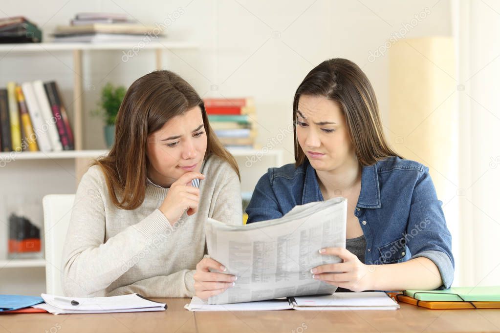 Front view portrait of two students finding suspicious news in a newspaper at home