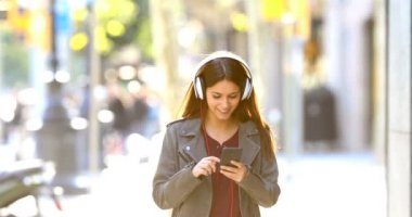 Sokakta müzik dinlerken kameraya doğru yürüyen bir mutlu genç önden görünümü