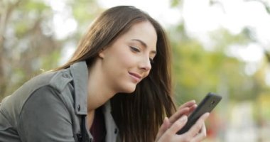 Yeşil bir arka plana sahip bir parkta oturan bir akıllı telefon kullanan rahat kadın