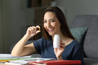 Elinde vitamin hapı tutan mutlu öğrenci gece geç saatlere kadar çalışıyor.