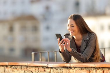 Mutlu kadın bir balkonda gün batımında akıllı telefon çevrimiçi içerik tarama