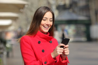 Kış yürüyüşlerinde kırmızı ceket giyen ve sokakta akıllı telefon kullanan mutlu bir kadın.