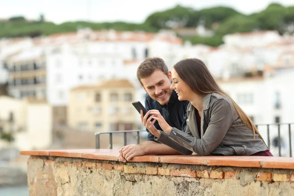 Casal Feliz Verificando Telefone Inteligente Uma Varanda Com Uma Cidade — Fotografia de Stock