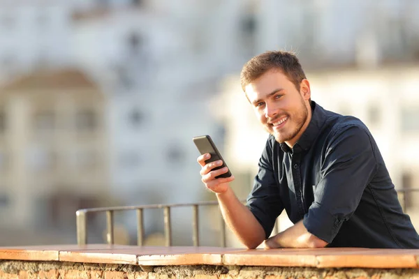 Szczęśliwy Człowiek Trzymając Smartfon Patrząc Kamery Balkon Zachodzie Słońca — Zdjęcie stockowe