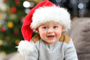 Noel Baba şapkası takan bebek Noel 'de evde kameraya bakıyor.