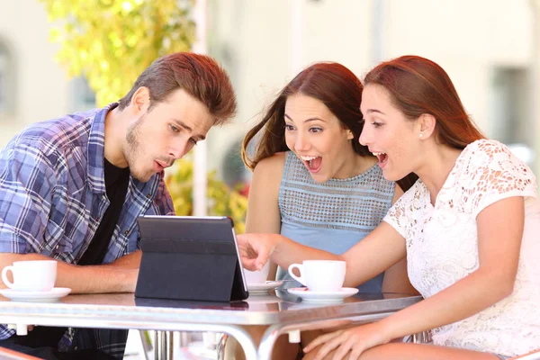 三个兴奋的朋友坐在咖啡店里看平板电脑的内容 — 图库照片