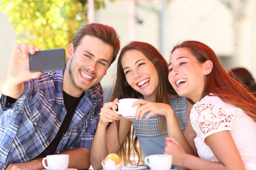 Three smiley friends taking selfies with a smart phone sitting in a coffee shop
