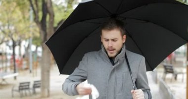 Kamera bir şemsiye yağmur altında tutan hapşırma doğru yürüyen hasta bir adam portresi önden görünüm