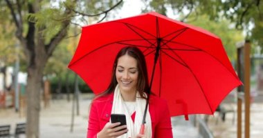 Akıllı telefon bir şemsiye yağmur altında tutan yürüyüş kontrol kırmızı mutlu bir kadın portresi önden görünüm