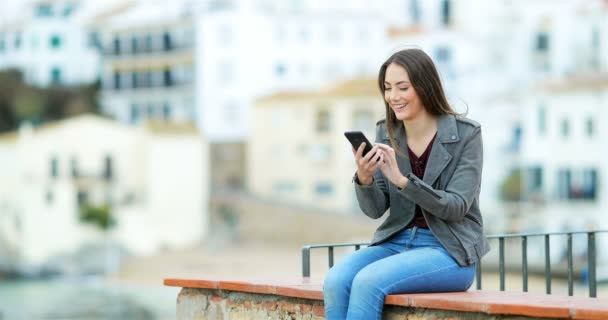 Happy Woman Using Smart Phone Sitting Ledge Coast Town Background — Stock Video