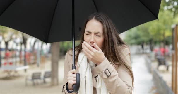 カメラはくしゃみの公園で傘を持って雨の下で歩いて歩いて病を患う女性の正面図 — ストック動画