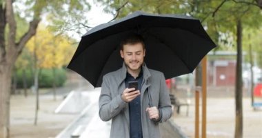Yağmur altında yürümek telefon konuşurken mutlu bir adam portresi önden görünüm