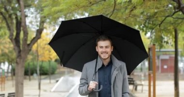 Bir şemsiye yağmur altında kışın tutan bir parkta yürüyüş mutlu bir adam portresi önden görünüm