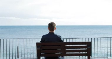 İzlerken okyanus plaj bir bankta oturmuş rahatlatıcı bir adam portresi arkadan görünüm