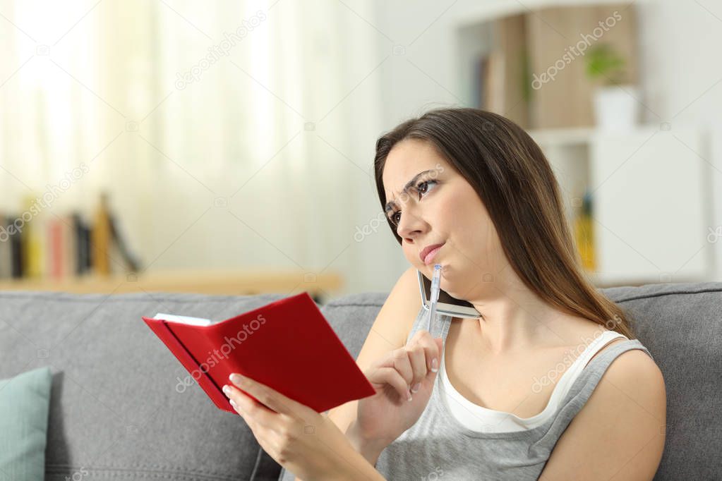 Confused woman on the phone holding an agenda sitting on a couch in the living room at home