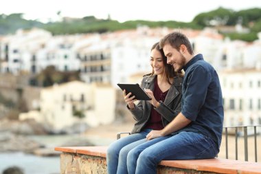 Mutlu çift tablet tatile bir sahil kasabasında kullanma bir çıkıntının üzerinde oturan