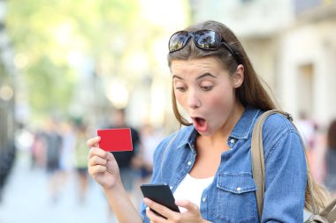 Şaşkın kız internetten alışveriş yapıyor ve sokakta akıllı bir telefondan teklif alıyor.