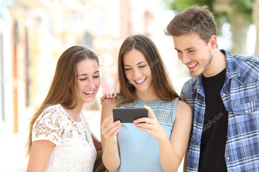 Three teenage friends watching media on a smartphone standing in the street