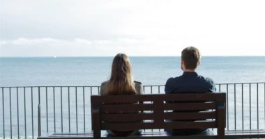 Arkadan görünüşü izlerken okyanus bir bankta oturan rahatlatıcı mutlu bir çift