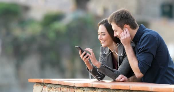 幸福的夫妇分享在线音乐从智能手机在农村公寓阳台 — 图库视频影像