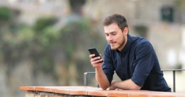 Mutlu adam akıllı telefon içeriğinde bir kırsal daire balkon izlerken