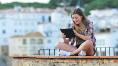 Mutlu genç kız tatilde bir çıkıntıya bir sahil kasabasında oturan tablet kullanma