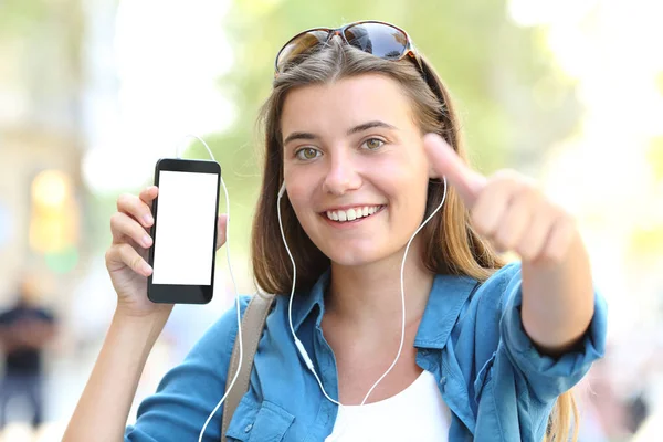 快乐的女孩听着音乐 在街上看到空白的智能电话屏风在为大拇指指引方向 — 图库照片