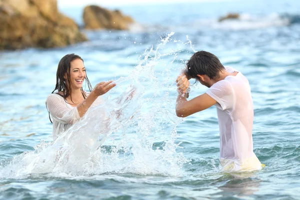一对自发性的夫妇开玩笑地在海滩上把水泡在海里 — 图库照片