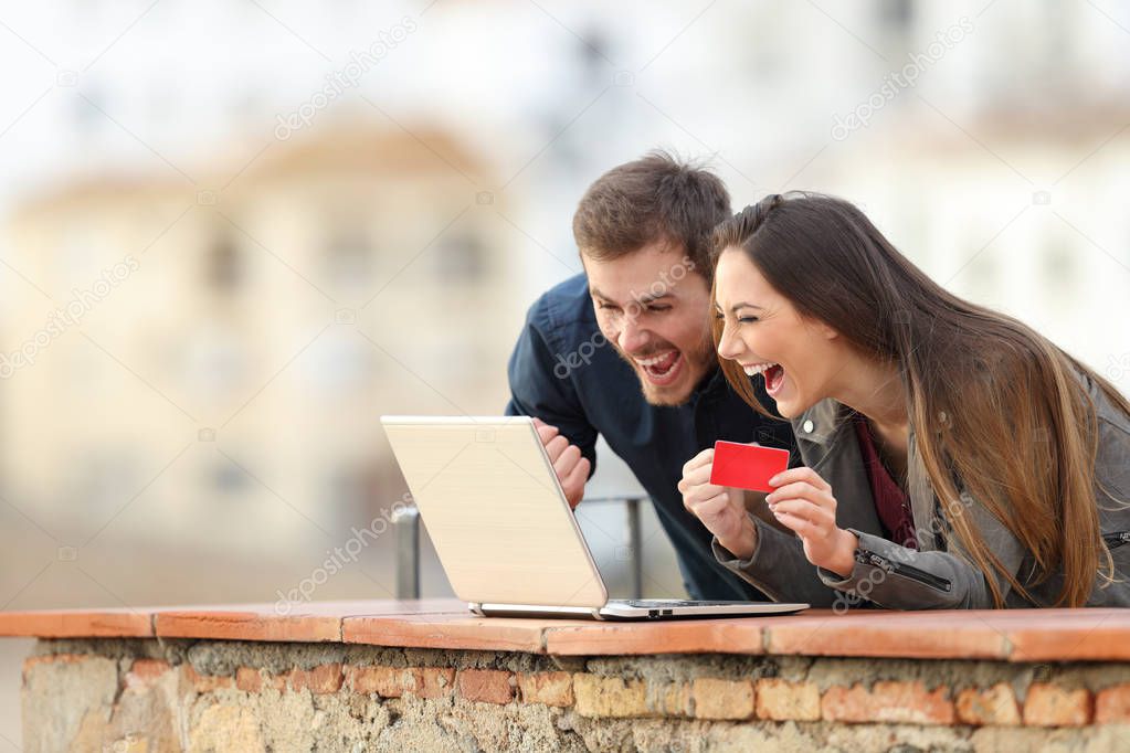 Excited online shoppers finding offers on a laptop in a balcony on vacation