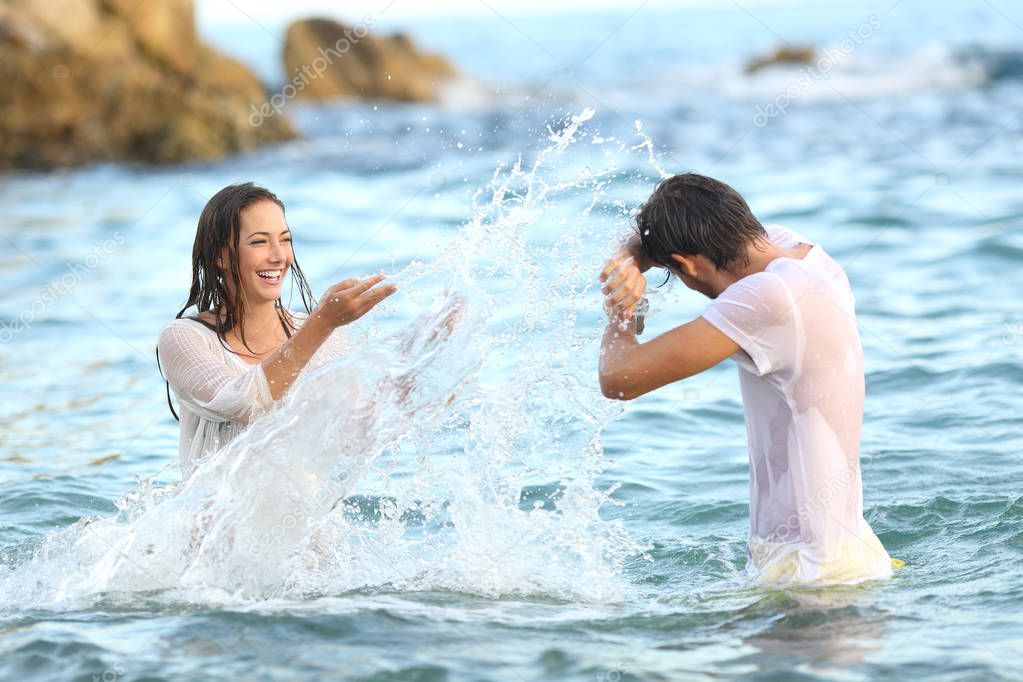Spontaneous couple joking throwing water bathing in the sea on the beach