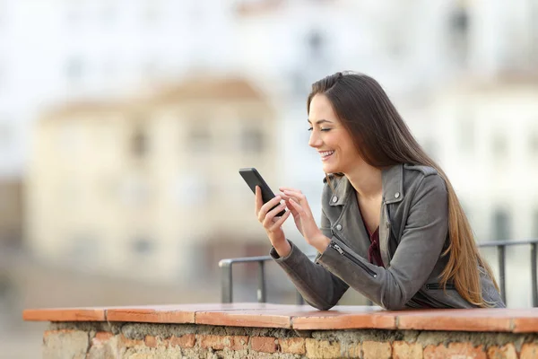 一个快乐的女孩在一个小镇的阳台上用智能手机度假 — 图库照片