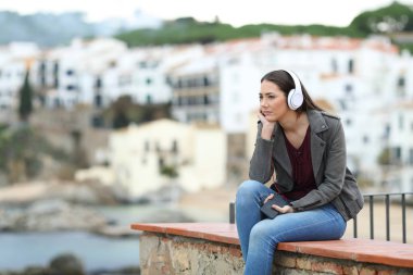 Kıyı kasabasında bir çıkıntıda oturmuş müzik dinleyen üzgün kadın.