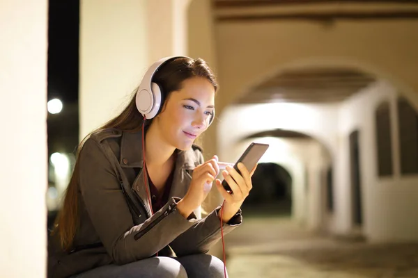 夜の街に座っているスマートフォンから音楽を聴くリラックスした女性 — ストック写真