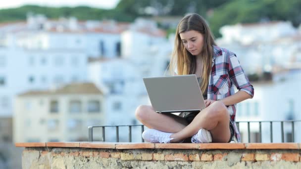 在一个小镇上坐在窗台上的笔记本电脑上写字的严重少女 — 图库视频影像