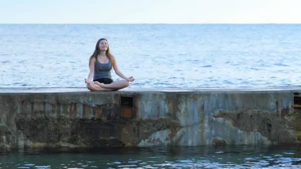 快乐的青少年练习瑜伽和呼吸在海滩上与海洋的背景 — 图库视频影像