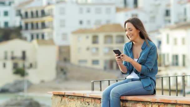Happy Woman Texting Smart Phone Outdoors Sitting Ledge Coast Town — Stock Video