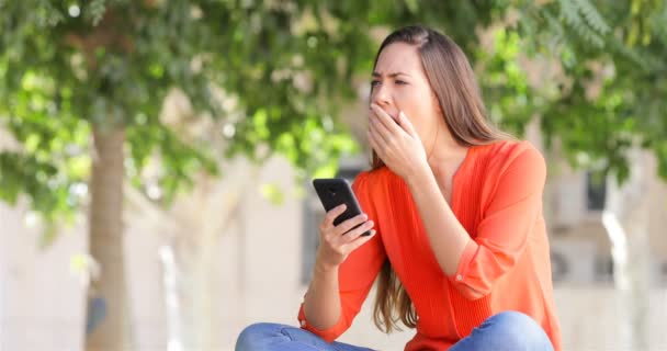 Mulher Bocejando Usando Telefone Inteligente Sentado Banco Parque — Vídeo de Stock