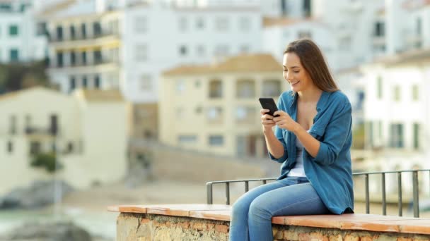 快乐的女人用智能手机 她的伴侣来了 在度假的时候坐在窗台上分享 — 图库视频影像
