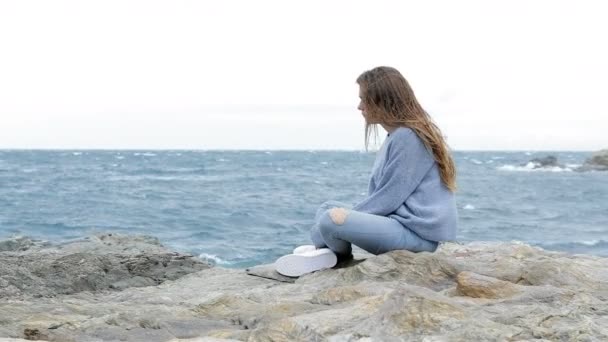 風の強い日にビーチに座っている悲しいティーンエイ ジャーの側面ビュー肖像画 — ストック動画