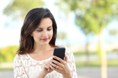 Güneşli bir günde bir parkta smartphone kullanarak rahat bir Bayan portresi